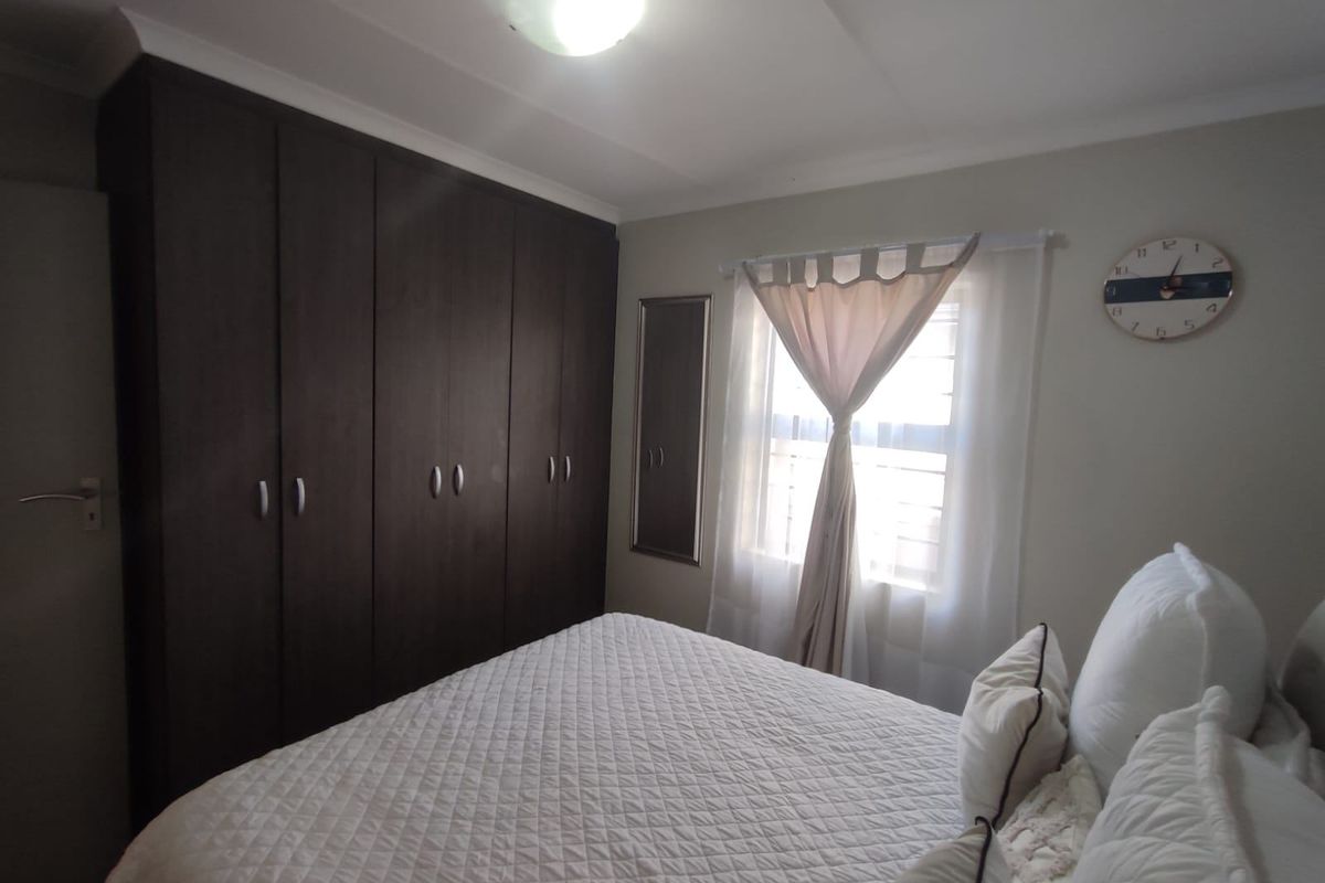 A well-maintained bedroom featuring dark wood built-in cupboards, neutral wall finishes, and a ceiling light fixture.