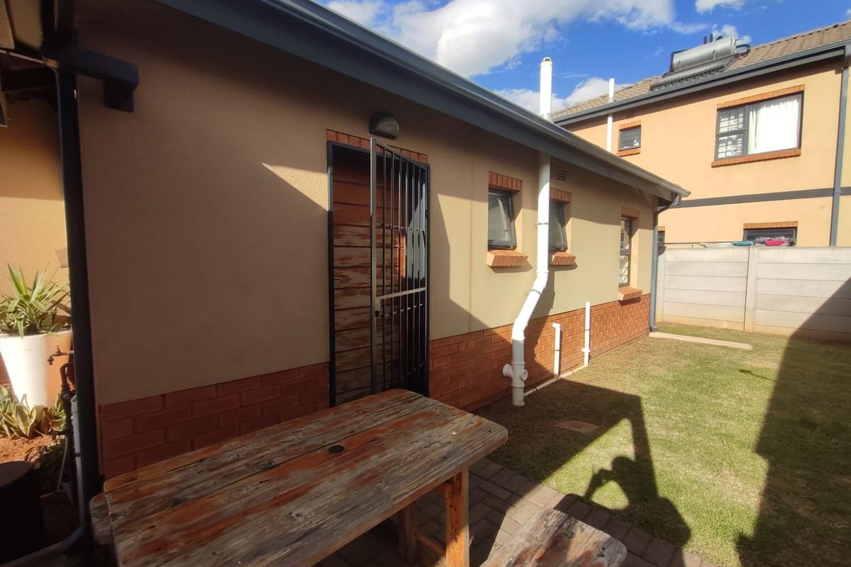 Rear exterior view of the property featuring a paved patio area, lawn, and access door with a security gate.