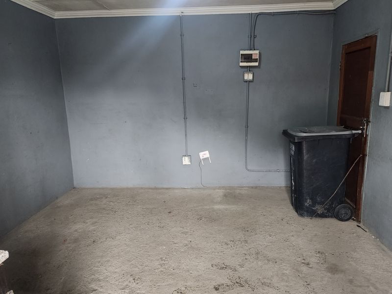 An empty garage space featuring exposed electrical conduit, a distribution board, and a concrete floor, suitable for storage or workshop conversion.