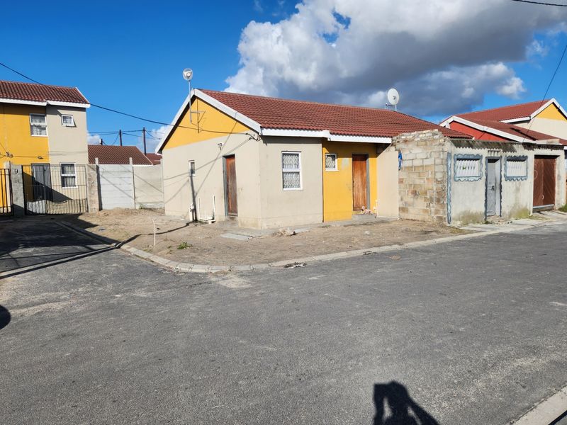Front exterior view of a single-story residential house featuring a tiled roof, concrete boundary wall, and basic security features.