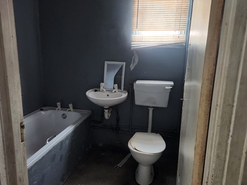 A small, dated bathroom featuring a bathtub, wall-mounted basin, and toilet, requiring significant renovation and cosmetic updates to improve its condition.
