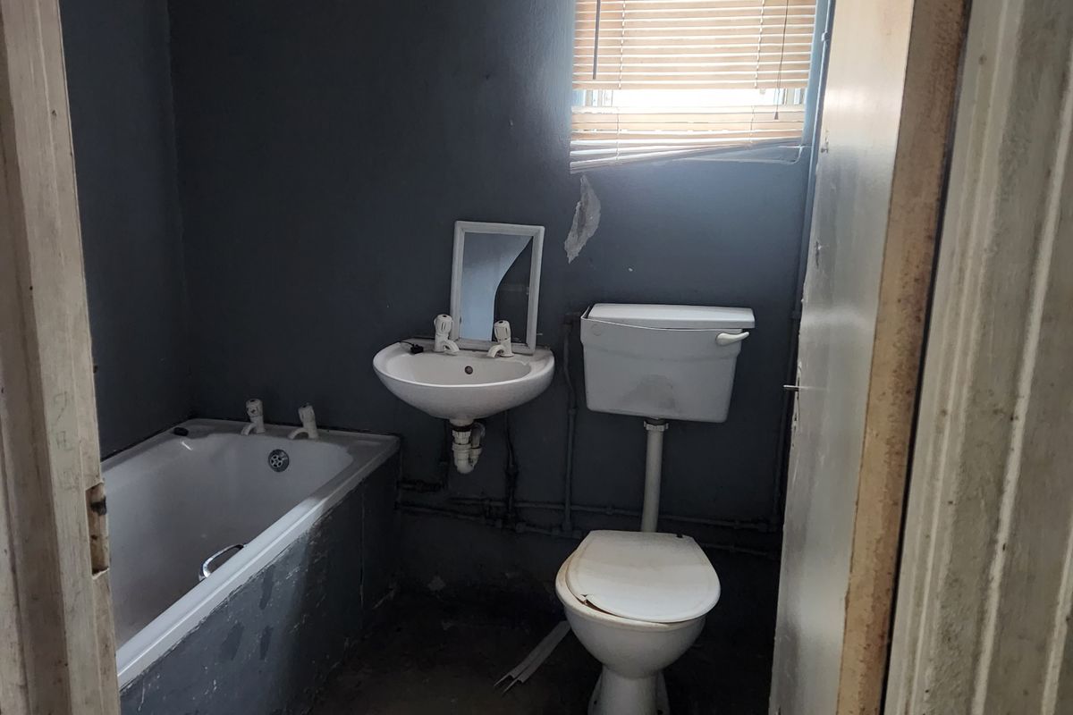 A small, dated bathroom featuring a bathtub, wall-mounted basin, and toilet, requiring significant renovation and cosmetic updates to improve its condition.