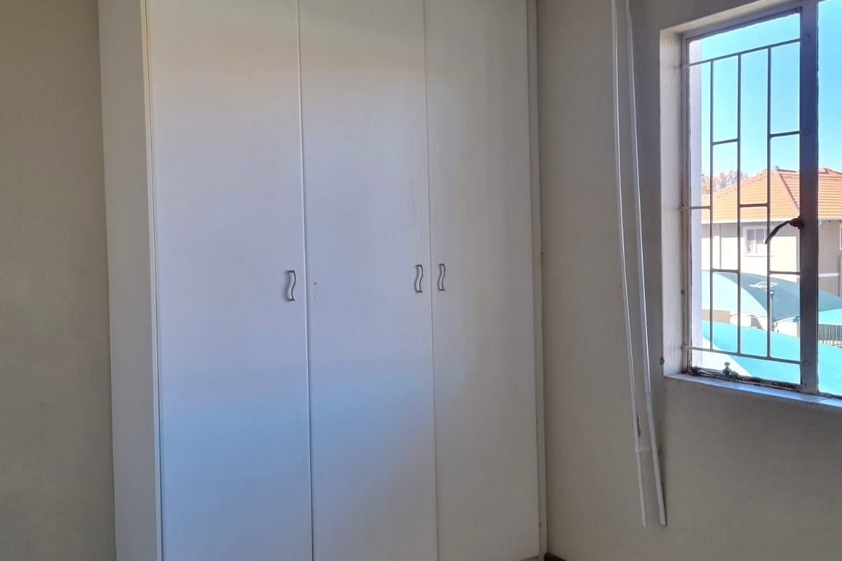 A vacant bedroom featuring tiled flooring, a built-in wardrobe, and a window fitted with security bars.