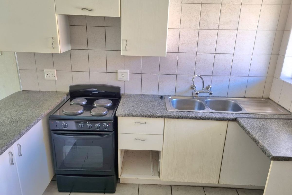 A functional kitchen featuring granite countertops, a double bowl sink, and a freestanding electric stove, with tiled splashbacks and cabinetry.