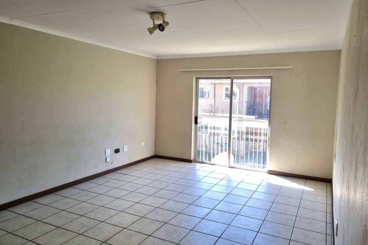 An empty living room featuring tiled flooring, neutral walls, and a sliding glass door providing access to an outdoor area.