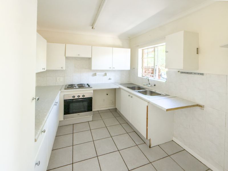 A functional, empty kitchen featuring white cabinetry, a built-in oven and hob, double sink, and tiled flooring, ready for a modern update.