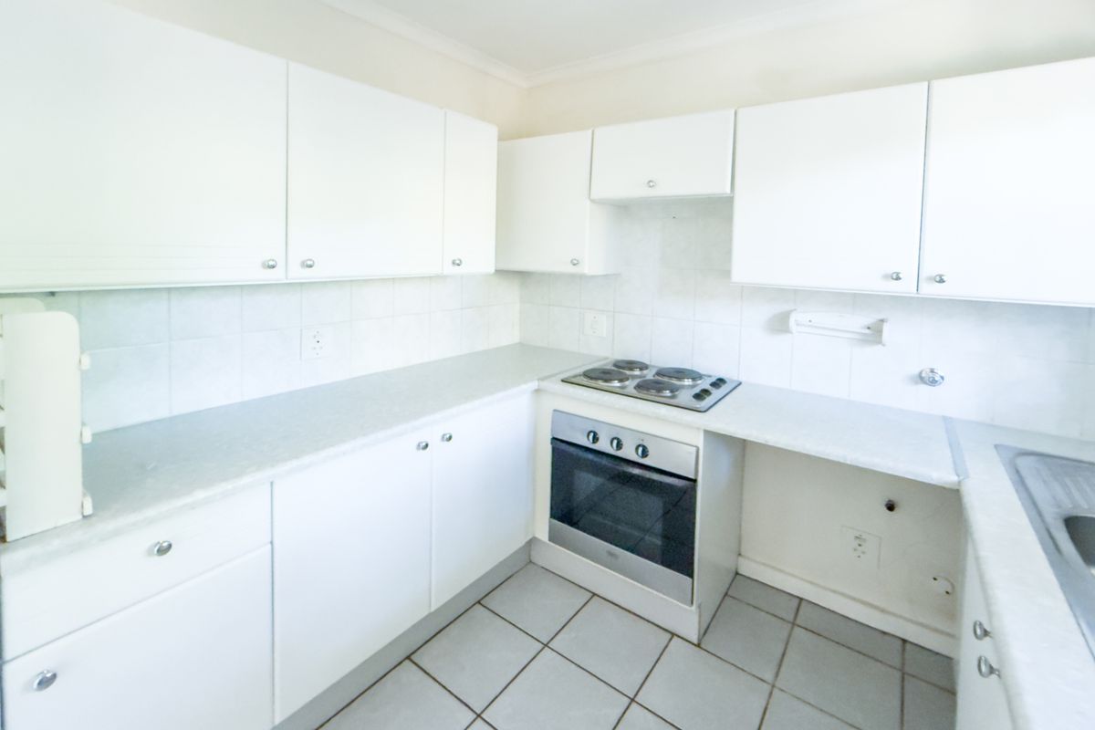 A functional kitchen featuring white cabinetry, laminate countertops, a built-in oven and hob, and tiled flooring.