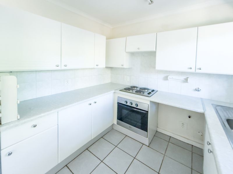 A functional kitchen featuring white cabinetry, laminate countertops, a built-in oven and hob, and tiled flooring.