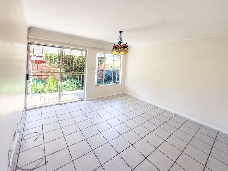 A bright, empty living room featuring neutral tiled flooring, a sliding glass door with security gate, and direct access to the garden area.