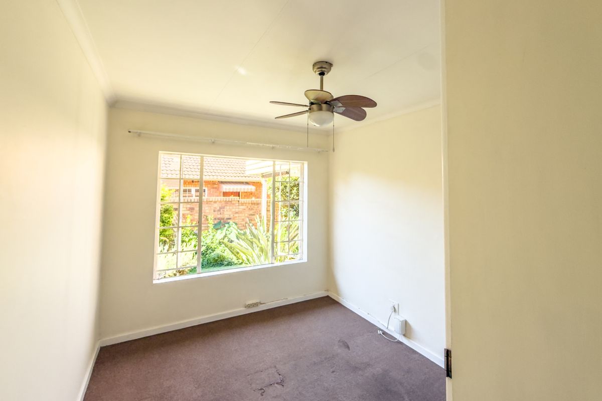An empty bedroom featuring a ceiling fan, grid-style window, and carpet flooring, offering a blank canvas for personalization.