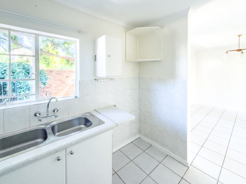A clean, functional kitchen area featuring a double bowl stainless steel sink, tiled splashbacks, and neutral ceramic floor tiles, ready for modern updates.