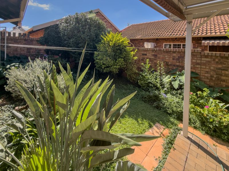 A private rear garden featuring a paved patio area, established landscaping, and brick boundary walls, viewed from under a covered patio.