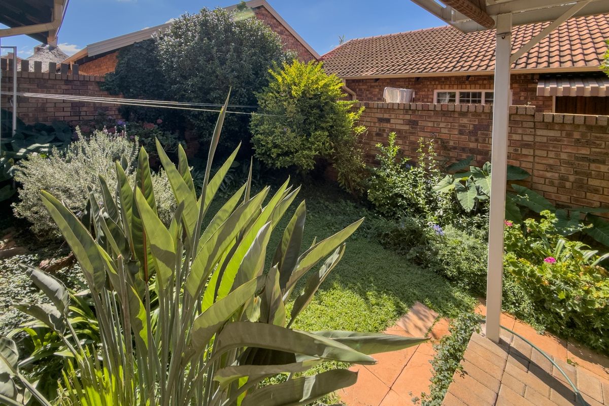 A private rear garden featuring a paved patio area, established landscaping, and brick boundary walls, viewed from under a covered patio.