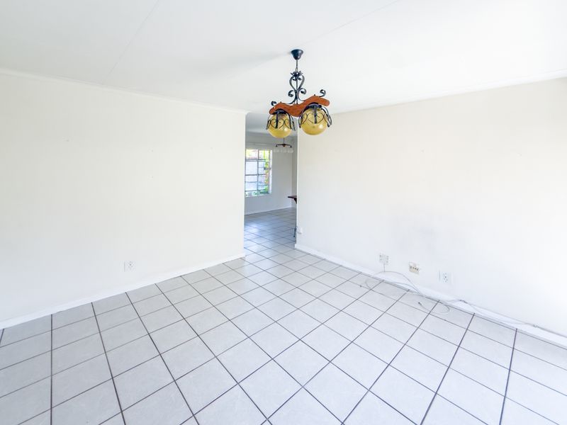 A bright, empty living area featuring neutral tiled flooring and a central ceiling light fixture, offering a blank canvas for interior design.