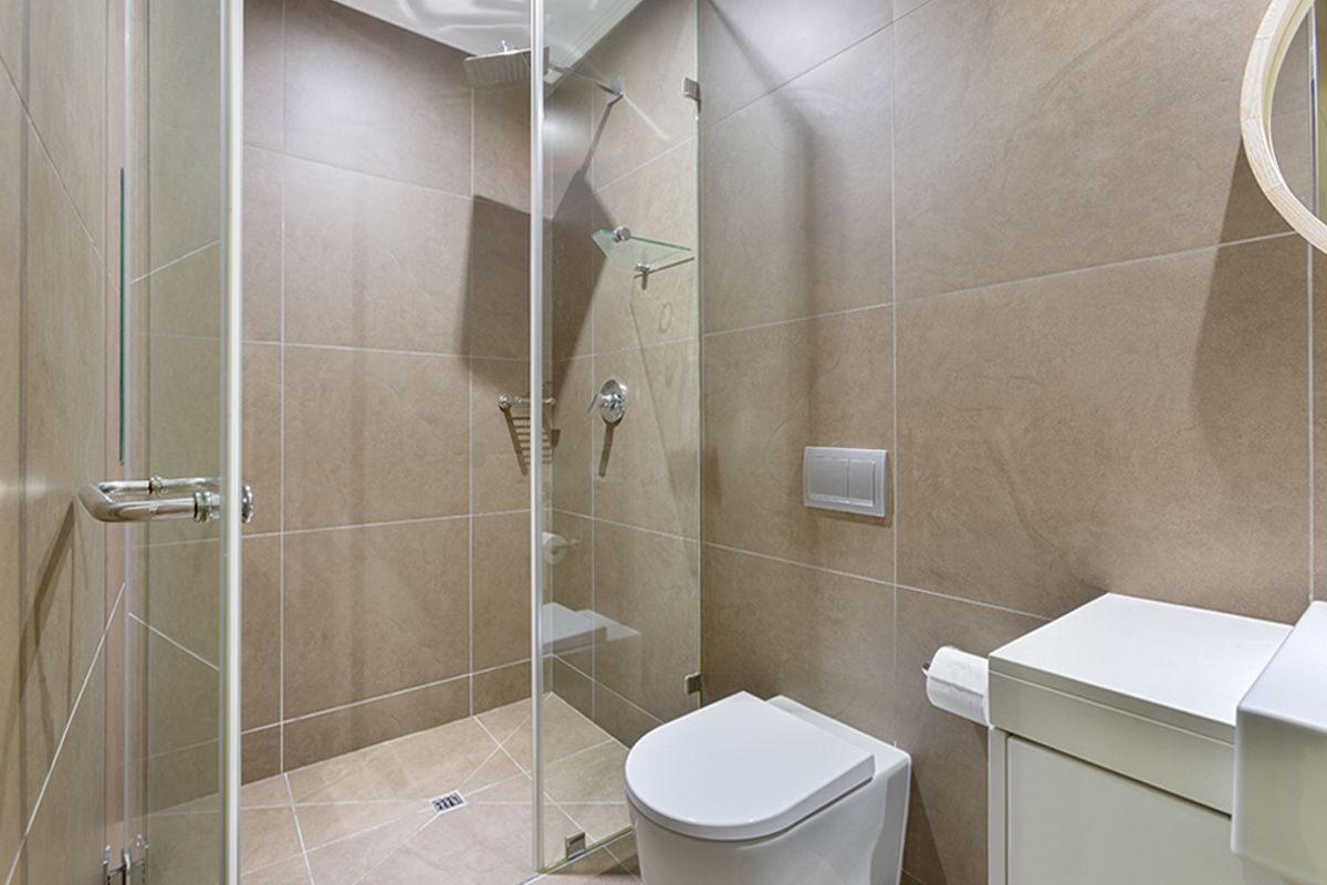 Modern bathroom featuring a walk-in shower with a glass screen, wall-mounted toilet, and neutral-toned floor-to-ceiling tiling.
