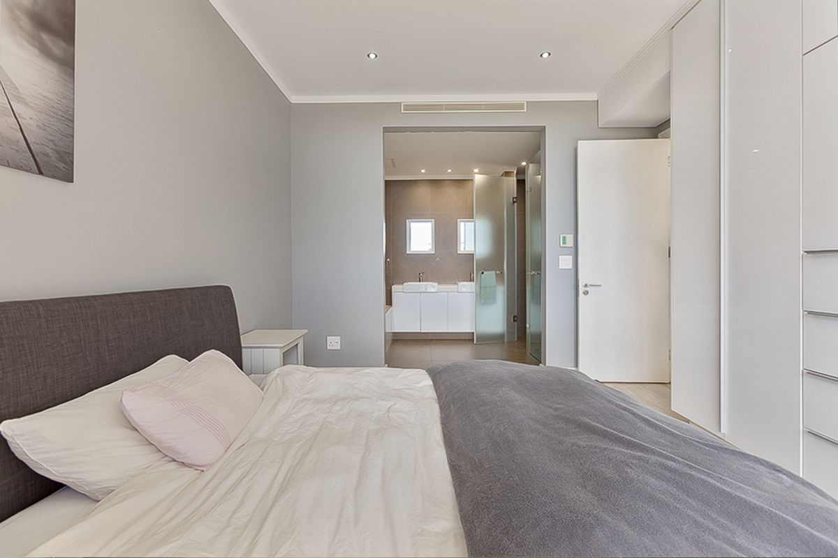 Modern bedroom featuring built-in cupboards, recessed lighting, and direct access to an en-suite bathroom with a contemporary vanity.