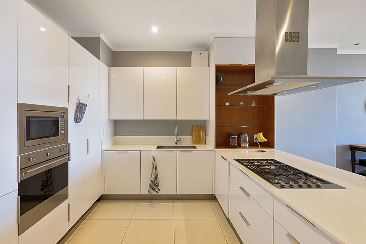 Modern kitchen featuring white gloss cabinetry, stone countertops, integrated stainless steel appliances, gas hob, and tiled flooring.