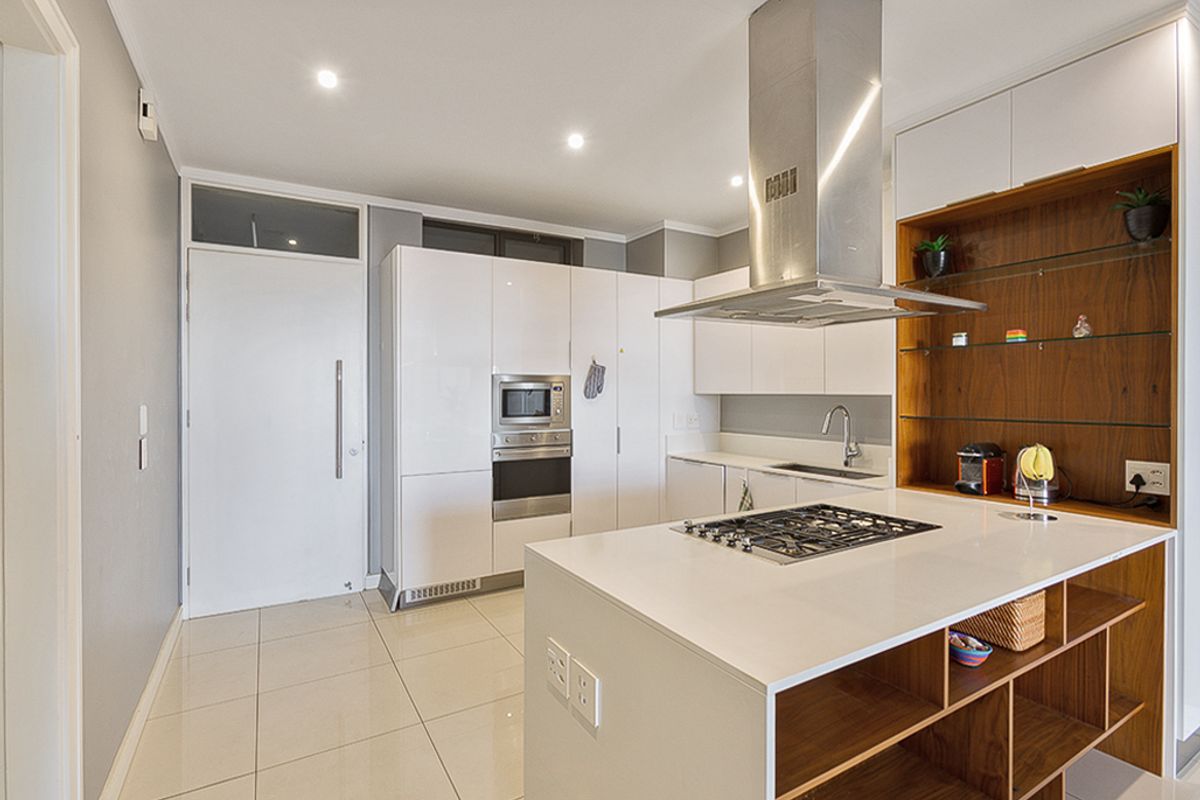 Modern kitchen featuring high-gloss cabinetry, stone countertops, a central island with a gas hob, and integrated stainless steel appliances.