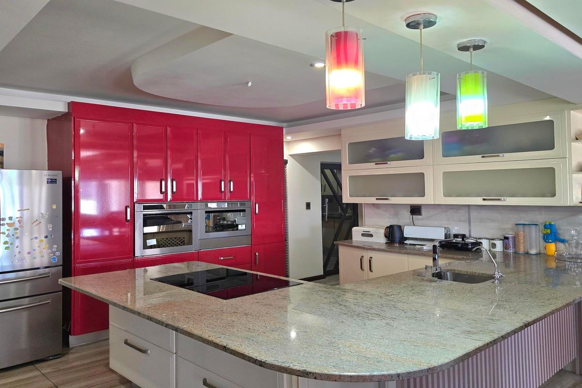 Modern kitchen featuring high-gloss red cabinetry, granite countertops, a central island with an induction cooktop, and integrated built-in appliances.