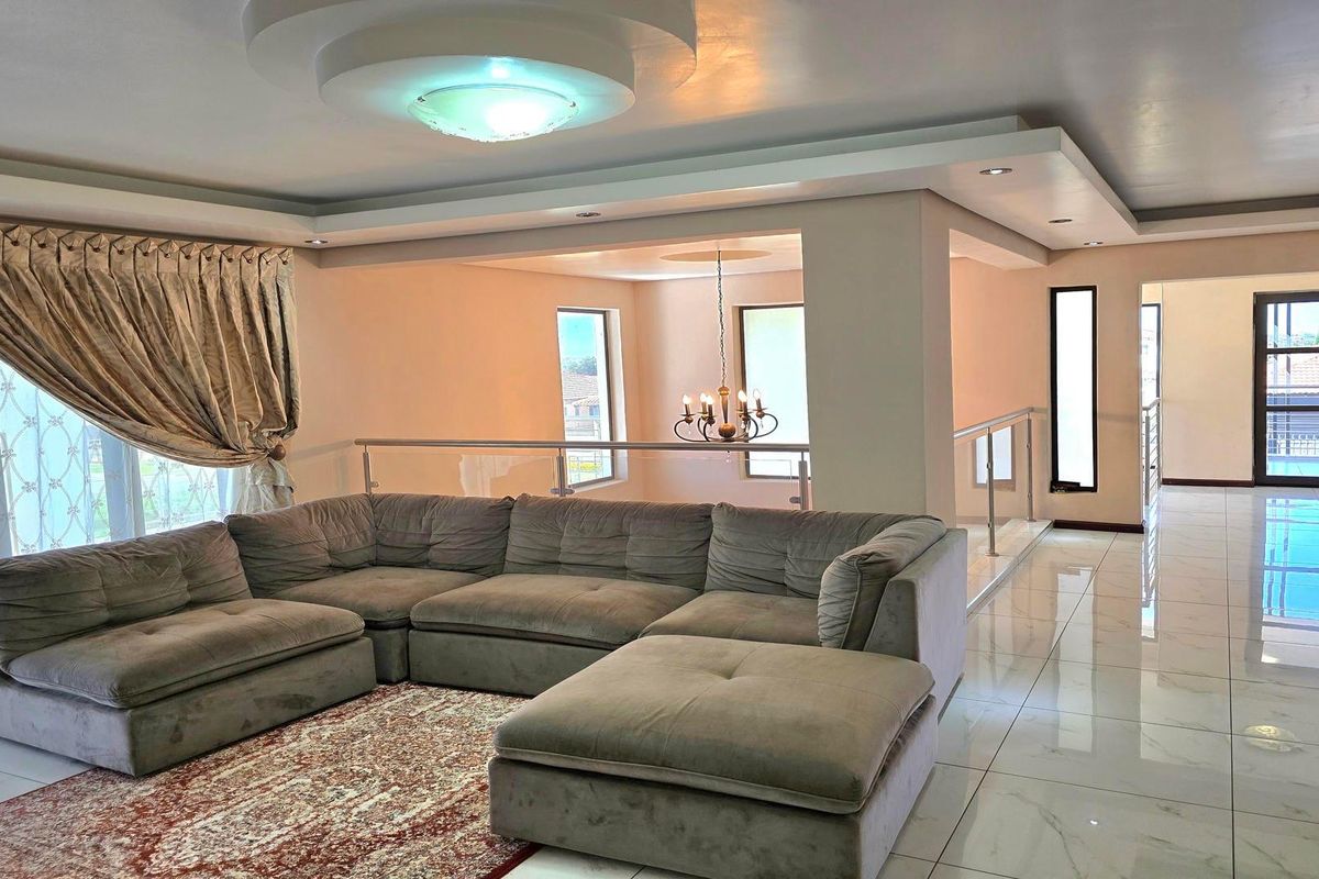 Spacious living area featuring modern porcelain floor tiles, recessed ceiling with cove lighting, and a glass balustrade overlooking the lower level.