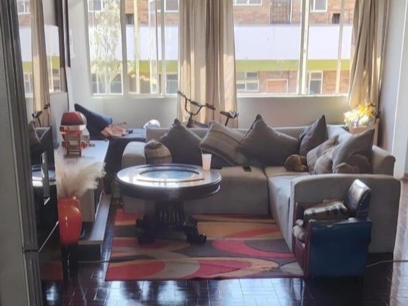 A living room featuring classic parquet flooring, a ceiling fan, and large windows that provide ample natural light.