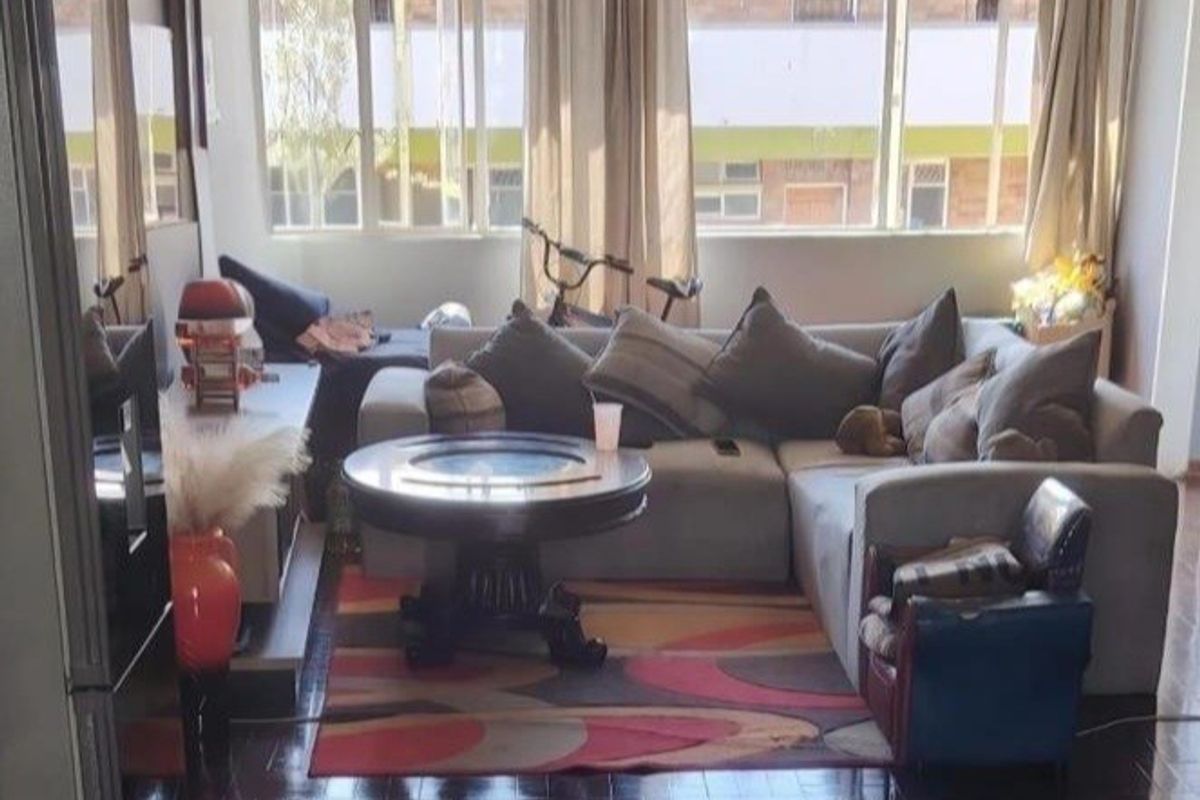 A living room featuring classic parquet flooring, a ceiling fan, and large windows that provide ample natural light.