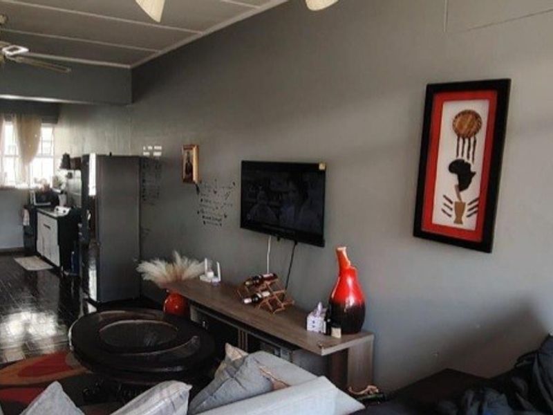 Open-plan living area featuring tiled flooring, a ceiling fan, and a wall-mounted television, providing a functional space that flows into the kitchen area.