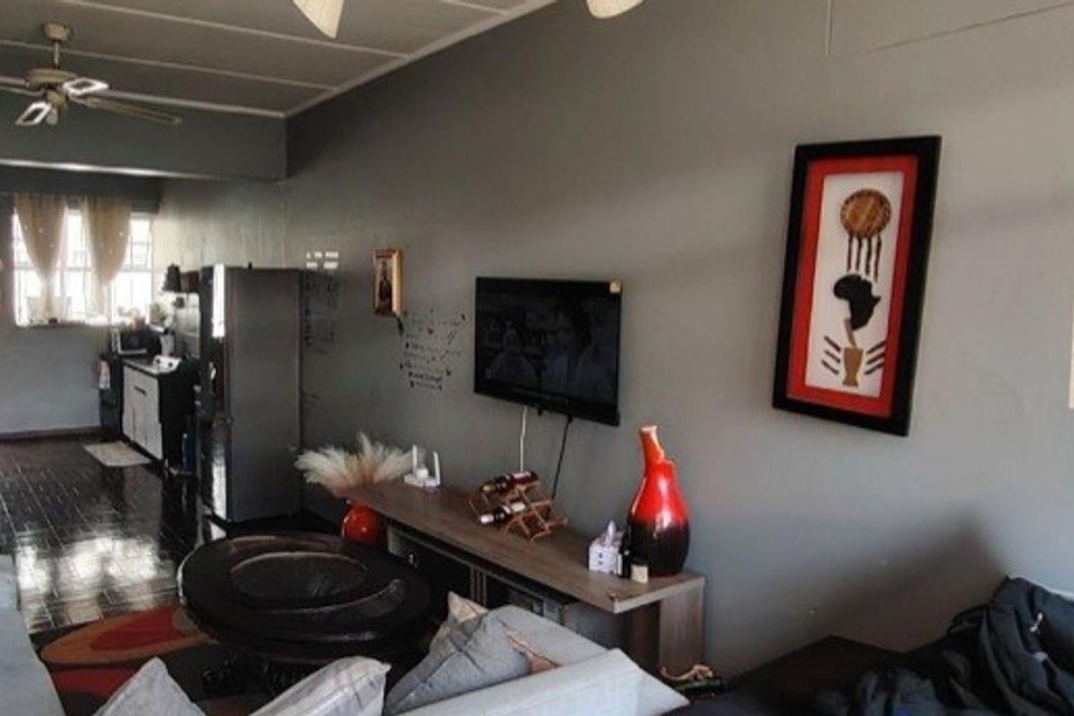 Open-plan living area featuring tiled flooring, a ceiling fan, and a wall-mounted television, providing a functional space that flows into the kitchen area.