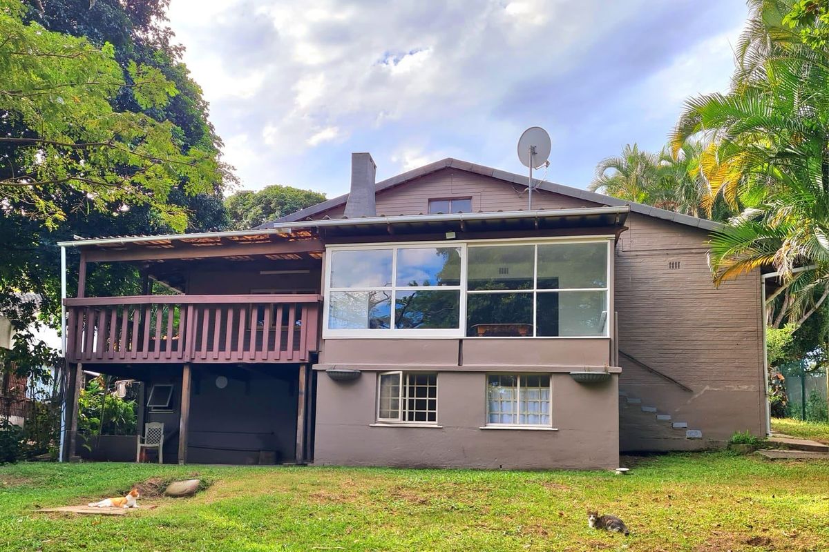 Rear view of the property featuring a raised timber deck, an enclosed sunroom, and a spacious garden area.