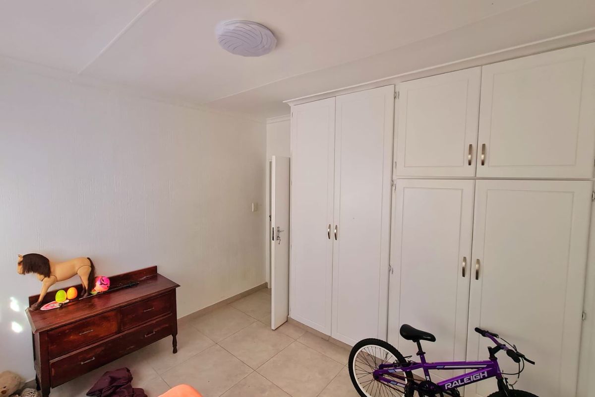 A bedroom featuring neutral tiled flooring and ample built-in cupboard storage with white cabinetry.