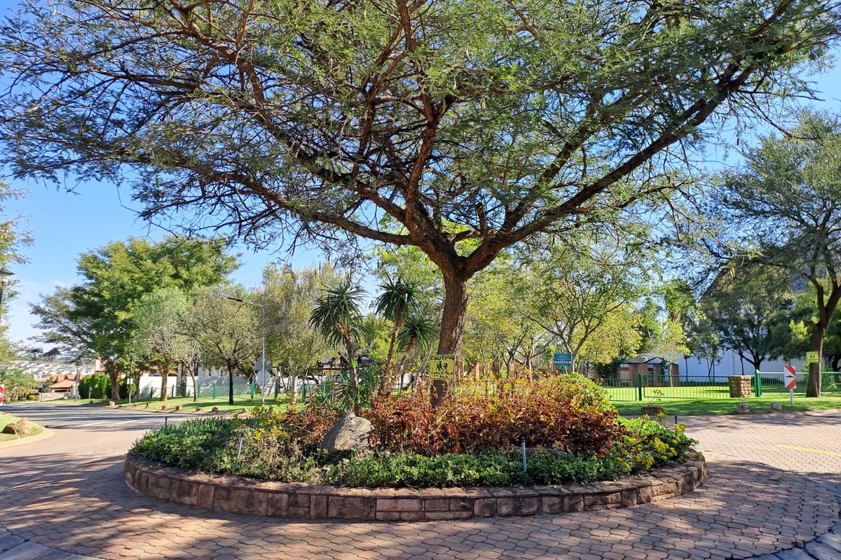 A well-maintained circular garden roundabout featuring mature trees, stone retaining walls, and established landscaping within a residential estate.