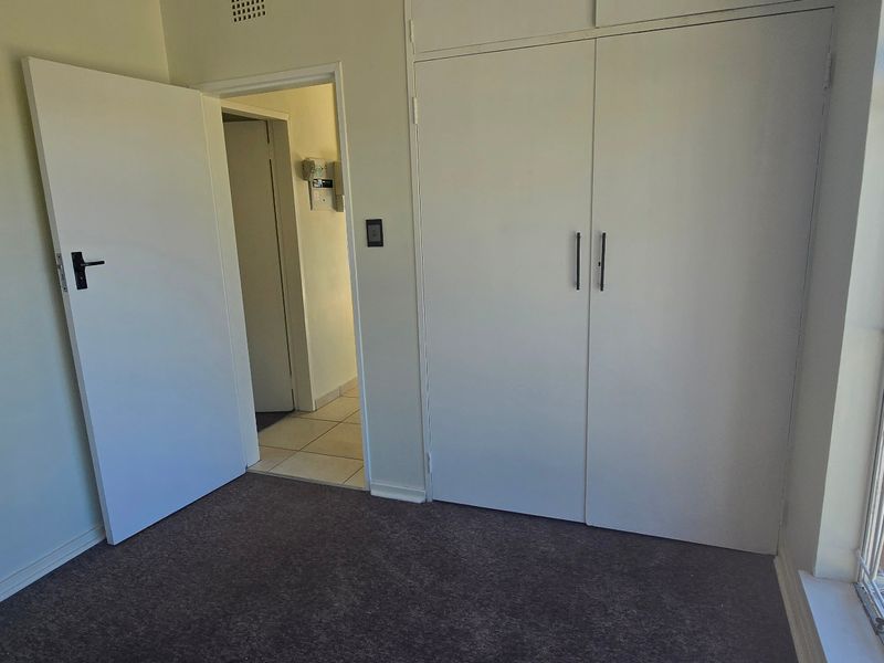 An empty bedroom featuring built-in cupboards, carpeted flooring, and a window with security bars, offering a clean and functional space.