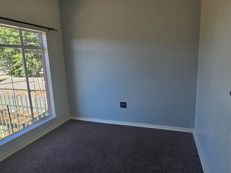 A bright, empty bedroom featuring carpeted flooring and a large window providing natural light and a view of the exterior.
