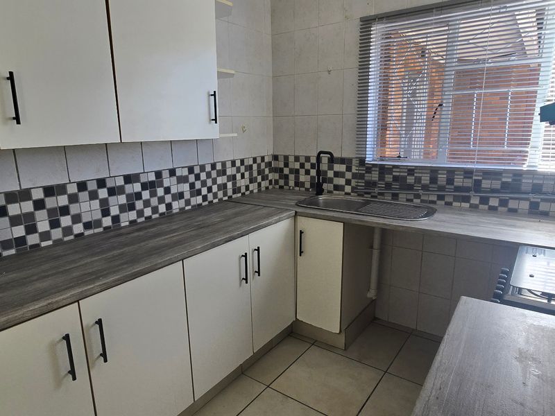 A functional kitchen featuring white cabinetry, wood-look laminate countertops, a tiled backsplash, and built-in cooking appliances with natural light from the window.