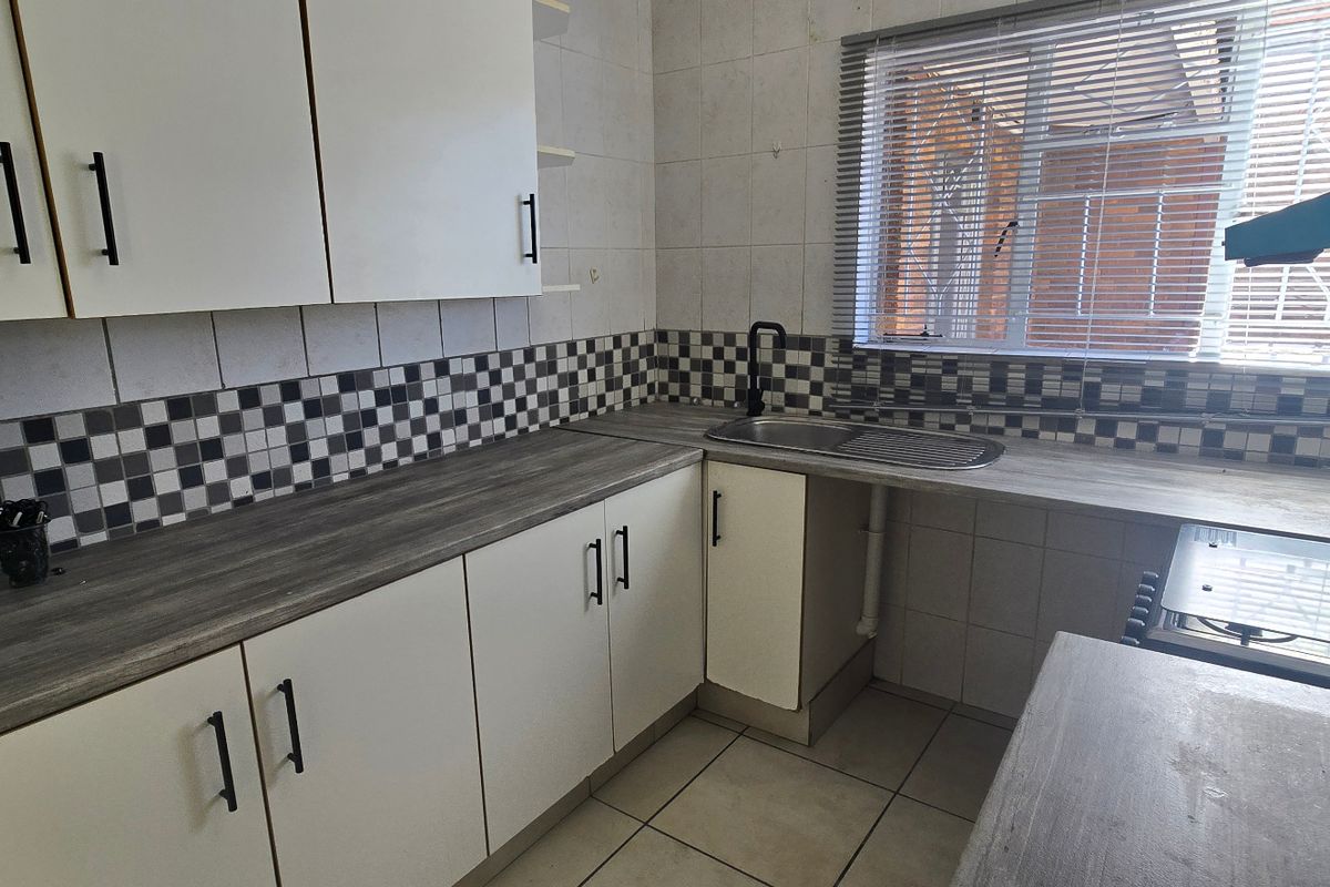 A functional kitchen featuring white cabinetry, wood-look laminate countertops, a tiled backsplash, and built-in cooking appliances with natural light from the window.