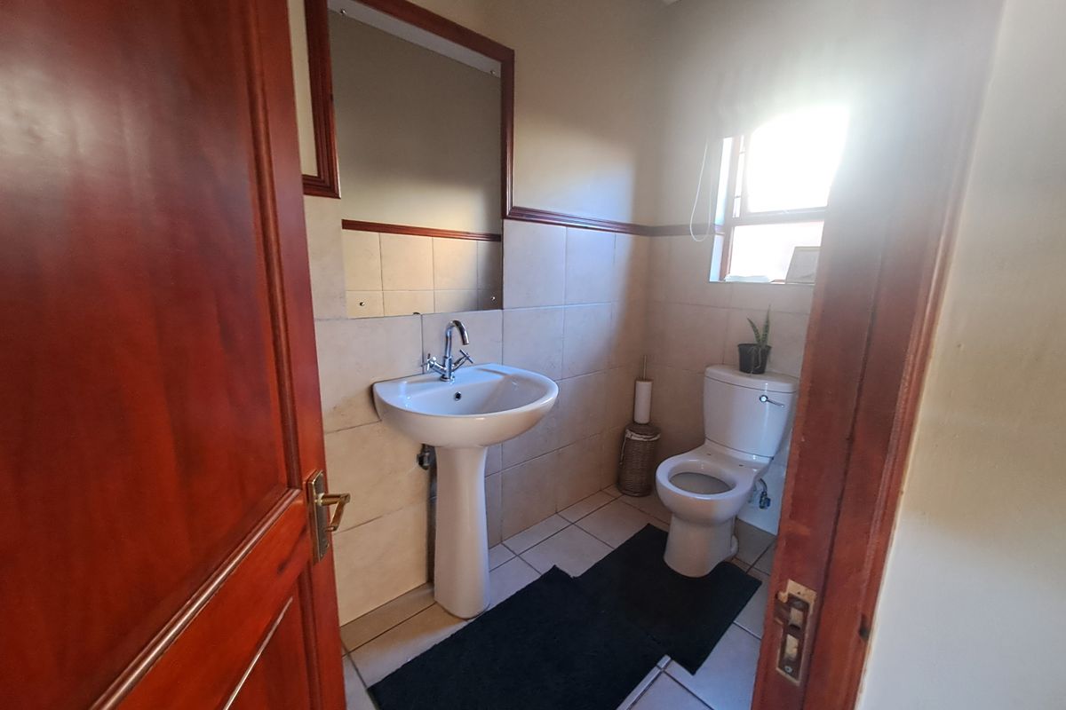 A functional guest bathroom featuring a pedestal basin, chrome mixer tap, wall-mounted mirror, and ceramic tiling throughout.