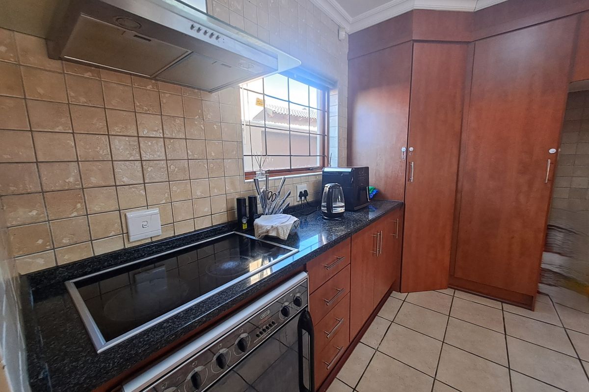 Functional kitchen featuring granite countertops, built-in oven with ceramic hob, extractor fan, and ample wooden cabinetry with tiled backsplash and flooring.