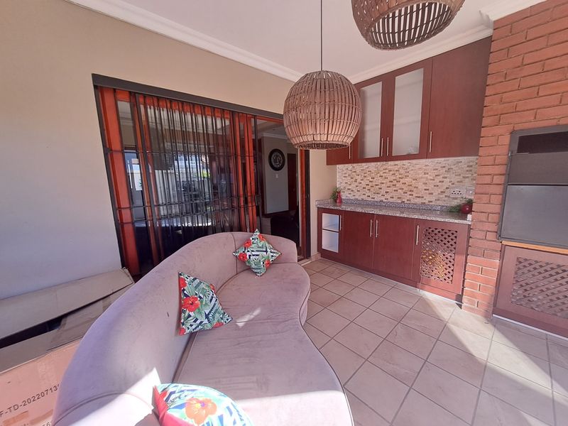 Covered patio area featuring a built-in braai, granite-topped cabinetry, mosaic backsplash, and tiled flooring, providing a functional outdoor entertainment space.