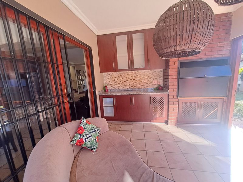Covered patio area featuring a built-in braai, granite-topped cabinetry, and tiled flooring, providing a functional outdoor entertainment space.