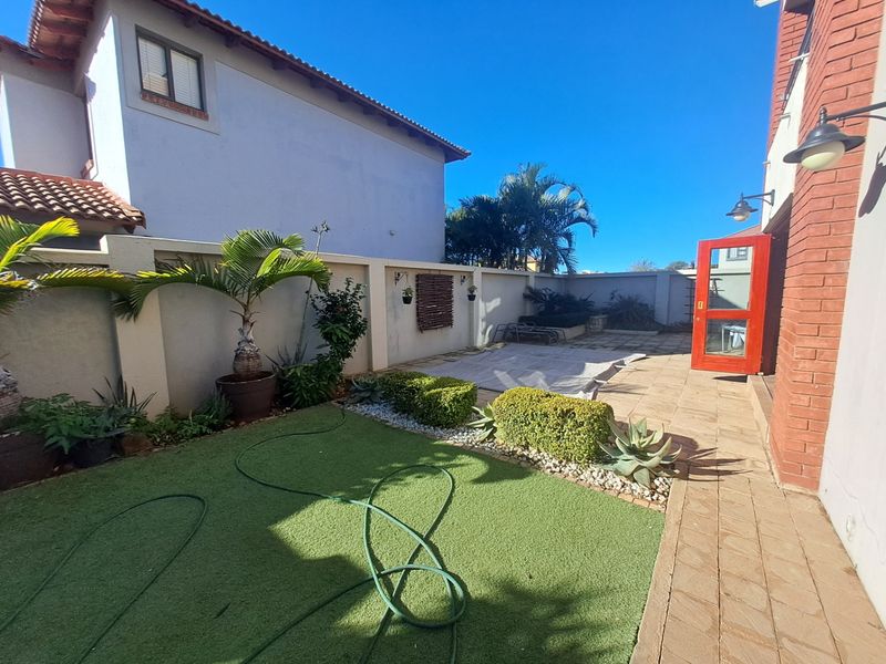 A private rear courtyard featuring a paved patio area, artificial lawn, and perimeter walling, providing a low-maintenance outdoor space.