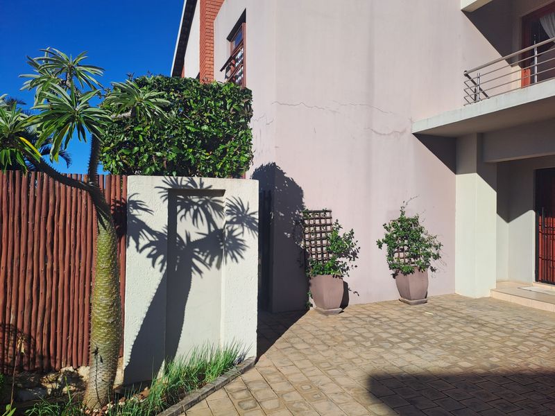 A view of the front exterior facade featuring a paved driveway, stucco wall finish, and a balcony with metal railings.