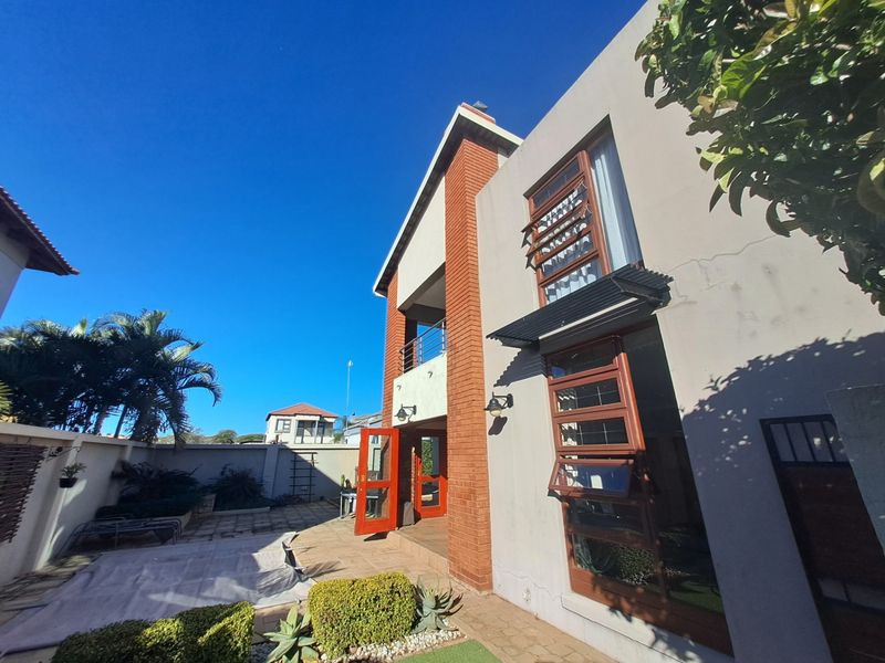 Rear view of the property featuring a brick and plaster facade, balcony, and paved patio area with established garden borders.