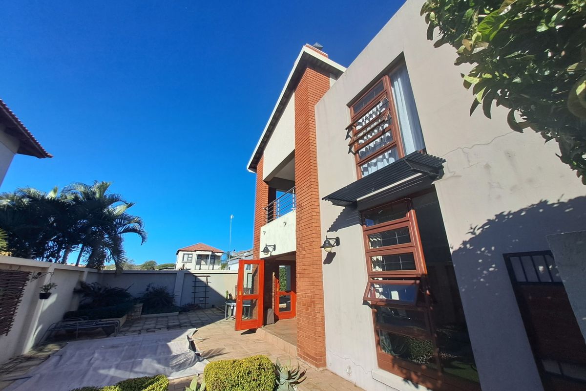 Rear view of the property featuring a brick and plaster facade, balcony, and paved patio area with established garden borders.