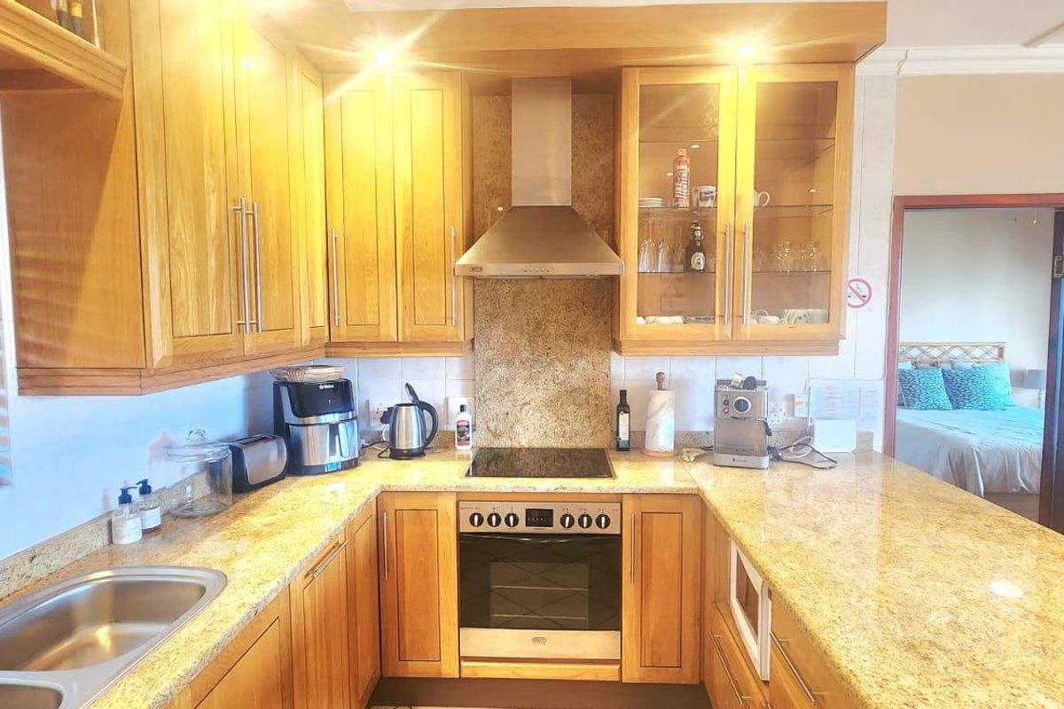 A functional kitchen featuring warm wooden cabinetry, granite countertops, a built-in oven with hob, and a stainless steel extractor fan.