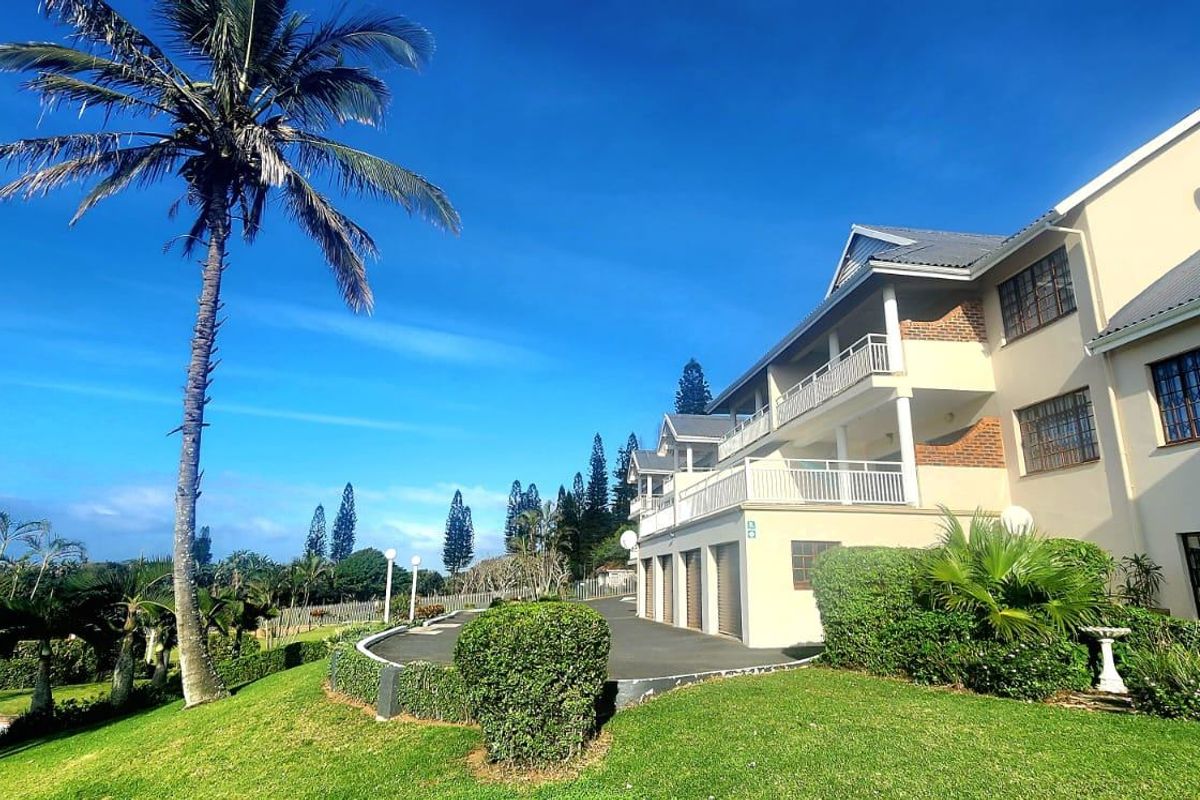 Rear view of the apartment complex featuring a multi-level facade, balconies, integrated garage doors, and well-maintained landscaped garden grounds.
