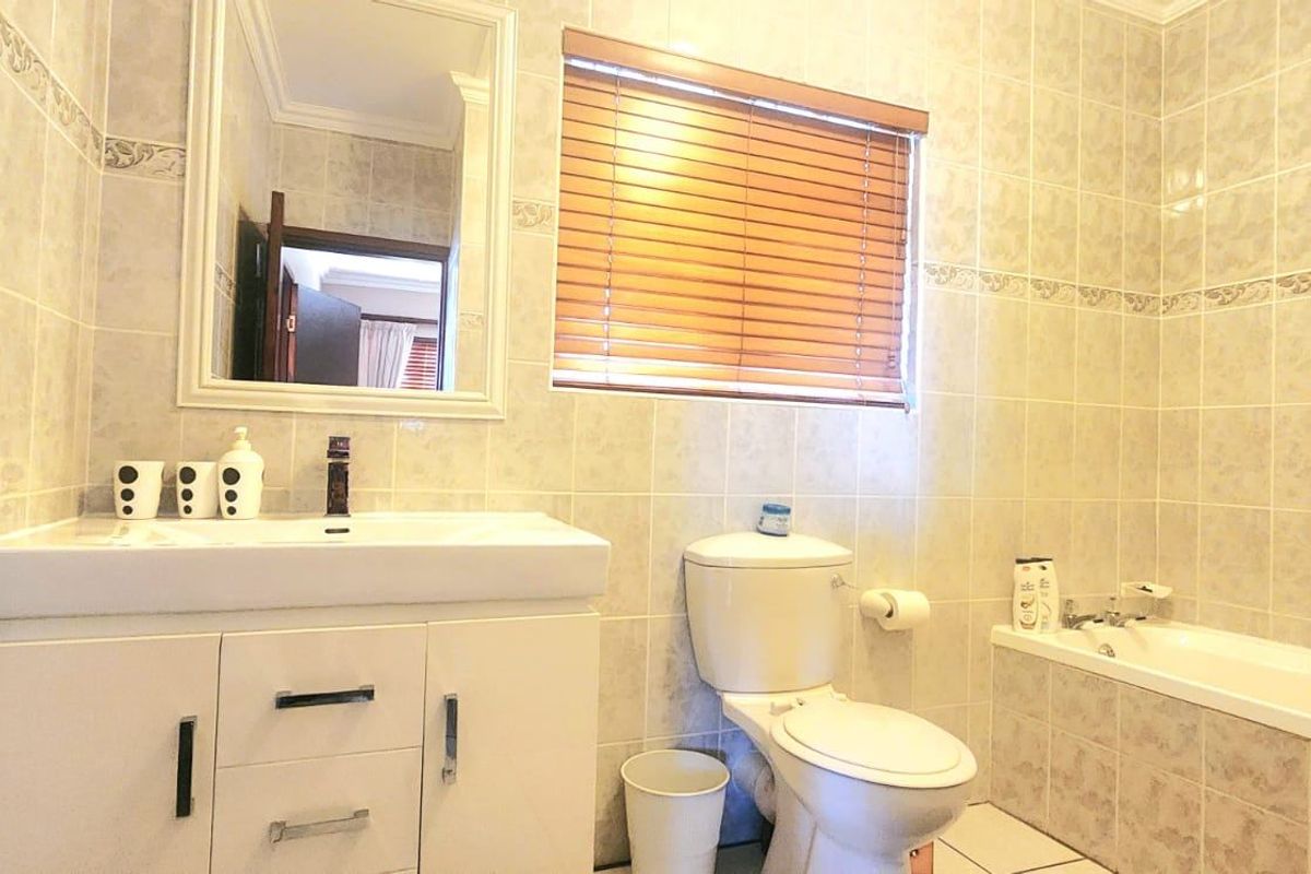 A functional bathroom featuring a vanity cabinet, wall mirror, toilet, and a bathtub with full-height wall tiling.