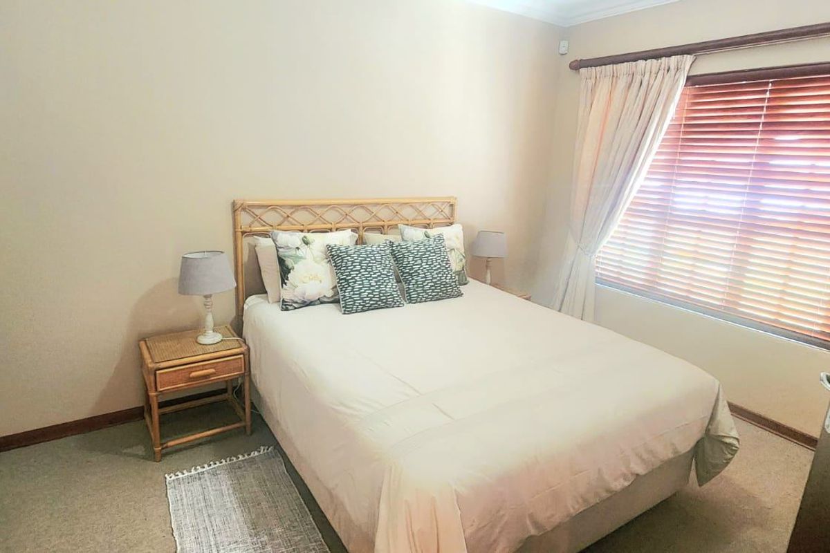 A functional bedroom featuring built-in wardrobes, carpeted flooring, and wooden venetian blinds, offering a neutral and comfortable living space.