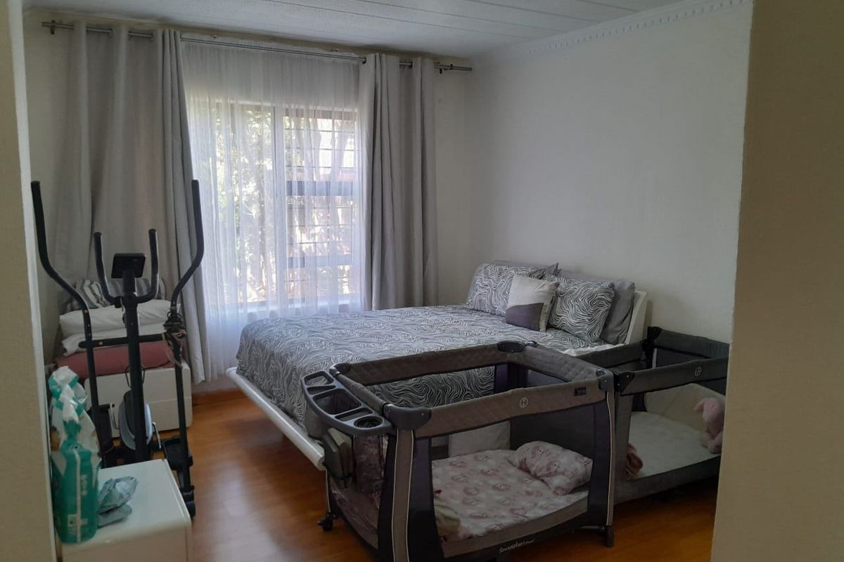 A bedroom featuring laminate flooring and large windows with curtain rails, providing natural light.
