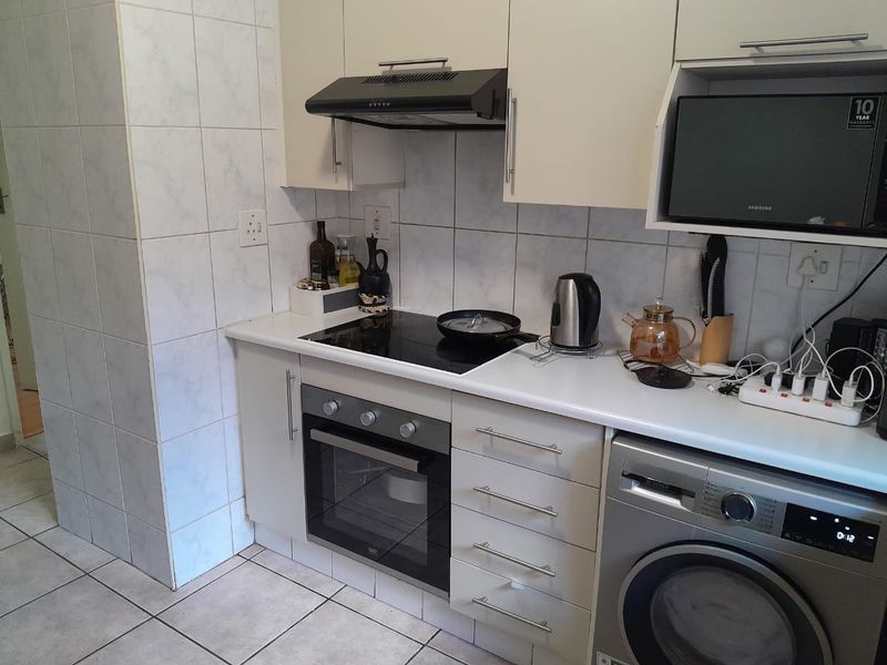A functional kitchen featuring built-in cabinetry, an electric hob, oven, extractor fan, and tiled finishes, providing a practical workspace for daily cooking.