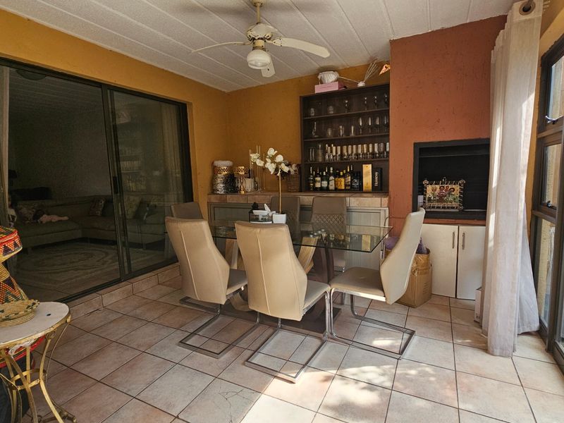 Covered patio area featuring tiled flooring, a built-in braai, ceiling fan, and sliding glass doors connecting to the interior living space.